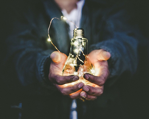 Person holding a lit lightbulb in their hands